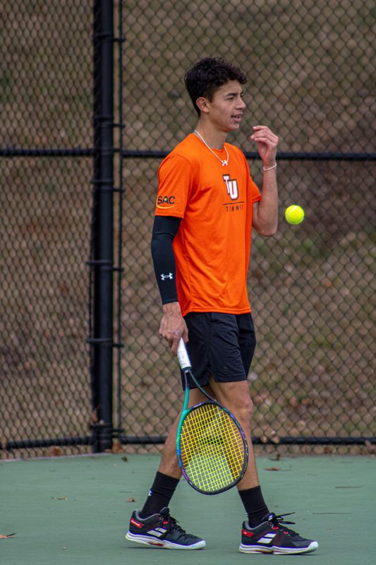 Felipe on a tennis court in an orange Tusculum jersey, racket in hand